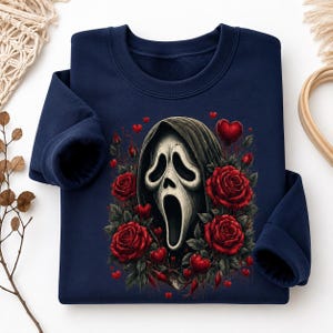 May include: A navy blue long-sleeve sweatshirt featuring a central graphic of a white ghost-like mask with a dark hood, surrounded by deep red roses and small red hearts scattered throughout the design on the front of the garment.