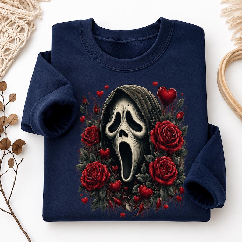 May include: A navy blue long-sleeve sweatshirt featuring a central graphic of a white ghost-like mask with a dark hood, surrounded by deep red roses and small red hearts scattered throughout the design on the front of the garment.