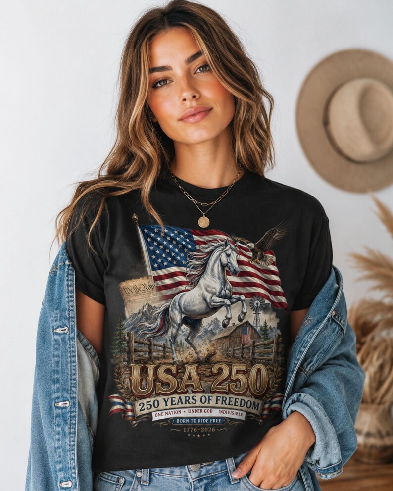 May include: A black t-shirt featuring a graphic of a rearing white horse, an American flag, a bald eagle, a barn, and a windmill. The text reads USA 250, 250 YEARS OF FREEDOM, ONE NATION UNDER GOD INDIVISIBLE, BORN TO RIDE FREE, and 1776-2026.