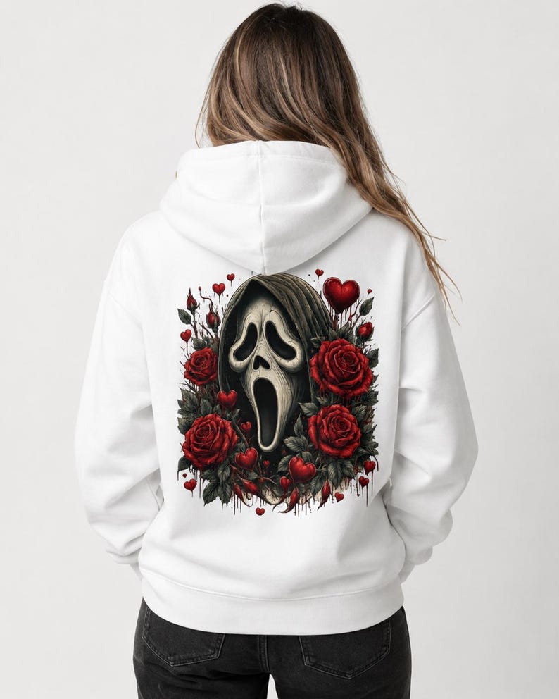 May include: A white hooded sweatshirt featuring a large graphic on the back. The design displays a central ghost-like mask with a dark hood, surrounded by deep red roses, green leaves, and small red hearts, with subtle dripping paint effects.