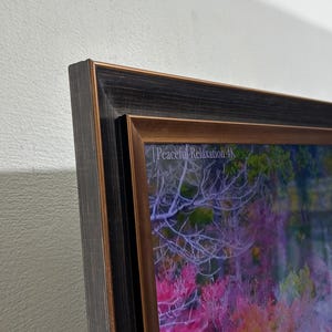 Op de afbeelding: Een ingelijst kunstwerk aan de muur met een donkere, getextureerde lijst en een bronskleurige binnenrand. De afbeelding toont een levendig landschap met felroze en oranje bladeren en de tekst Peaceful Relaxation 4K in de hoek.