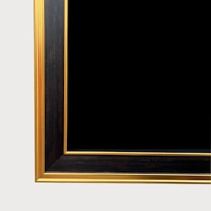 Peut inclure: Gros plan sur un cadre noir rectangulaire avec un bord intérieur doré et un bord extérieur marron foncé. Le cadre est posé sur un fond blanc.