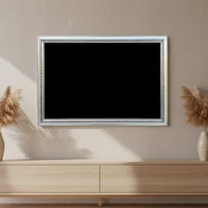 Könnte beinhalten: Ein großer, rechteckiger Fernseher mit silbernem Rahmen hängt über einem hellen Holzschrank. Zwei passende Vasen mit getrocknetem Pampasgras sind auf beiden Seiten des Fernsehers platziert. Die Wand ist in einem neutralen Beigeton gestrichen.