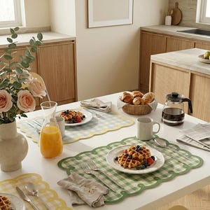 Può includere: Un tavolo per la colazione apparecchiato con waffle, frutta e succo d'arancia. Il tavolo è apparecchiato con tovagliette a quadretti, piatti, posate e una caffettiera. Un vaso di fiori e un cestino di pane completano la scena.