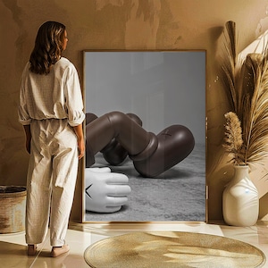 May include: A framed artwork featuring a brown and white cartoon figure in a relaxed pose. The figure has large, rounded features and a stylized appearance. The artwork is displayed in a room with neutral tones and decorative elements.