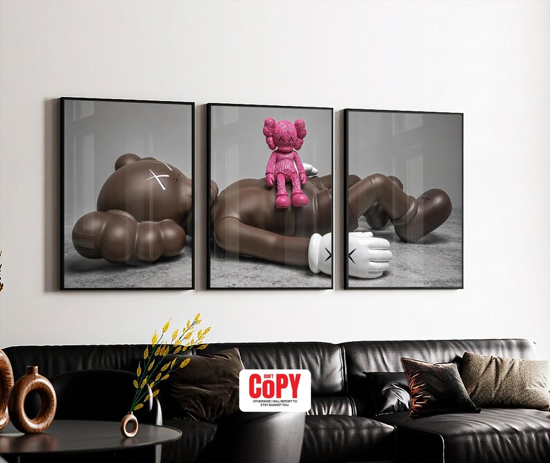 May include: Triptych wall art featuring three framed prints. Each print showcases a brown figure in a relaxed pose, with a pink figure atop one. The figures have white gloves and a white 'X' on the head. The artwork is displayed above a black leather sofa.