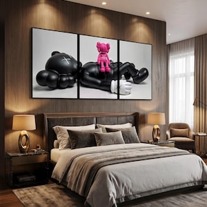 May include: A triptych wall art set featuring a large black character with white X-shaped eyes lying down, with a smaller bright pink character sitting on its chest. The figures have rounded limbs and white gloved hands against a plain background.