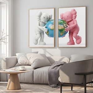 Peut inclure: Deux impressions encadrées représentant des personnages de dessins animés tenant des globes. L'une montre une figurine blanche, l'autre une figurine rose. Les personnages ont des yeux en forme de X et sont sur fond blanc. Les impressions sont dans un salon.