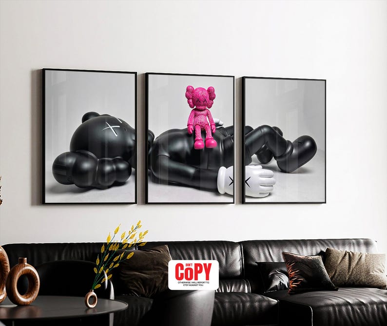 May include: A triptych wall art set featuring a large black KAWS-style character lying down, with a smaller bright pink KAWS-style figure sitting on its chest. The black figure has white gloved hands and X-shaped eyes, while the pink figure is solid.