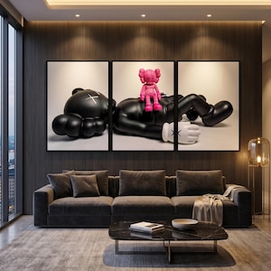 May include: A triptych wall art set featuring a large black cartoon-style figure lying down with an X-shaped mark on its head, while a smaller bright pink figure sits on its chest. The figures have white gloved hands with X-shaped markings.