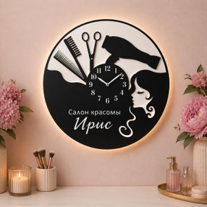 May include: A black and white wall clock with a salon theme. The clock features a silhouette of a woman's face, a comb, scissors, and a hair dryer. The clock face has the text "Salon of Beauty Iris".