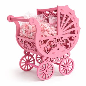 May include: A pink wooden baby carriage filled with pink and white sweets in clear bags. The carriage features decorative cutouts and spoked wheels. The carriage is a light pink colour and is on a white background.