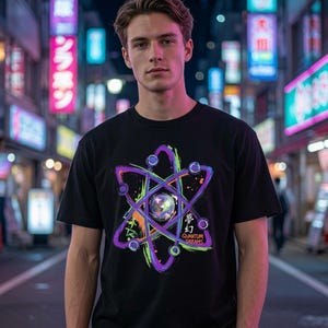 May include: A black short-sleeved t-shirt featuring a colourful graphic of an atom with purple, blue, and orange brushstroke accents. The design includes a central sphere and the text "QUANTUM DREAMS" with Japanese characters printed below it.