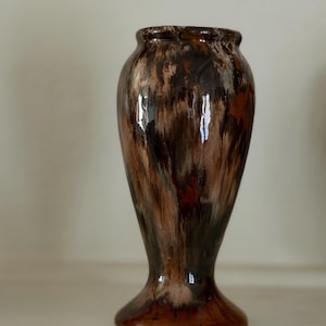 May include: A ceramic vase with a glossy finish featuring a marbled pattern of dark brown, black, and cream colors. The vase has a narrow neck that flares out toward the rim and a wide, circular base, creating a smooth, curved silhouette.