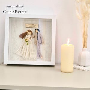 Könnte beinhalten: Ein gerahmtes personalisiertes Paarporträt mit Garnpuppen eines Brautpaares. Die Braut trägt ein weißes Kleid und hält einen Blumenstrauß. Der Bräutigam trägt einen Anzug. Der Rahmen enthält den Text "Emma & Liam June 14, 2016".