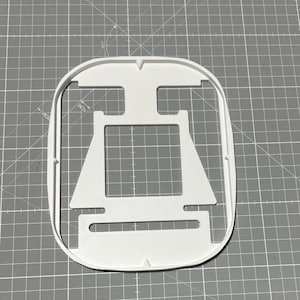 Peut inclure: Un emporte-pièce en plastique blanc en forme de voilier. Le découpoir a un centre rectangulaire avec une voile triangulaire et un bord extérieur arrondi. Le découpoir est sur un tapis de coupe gris.