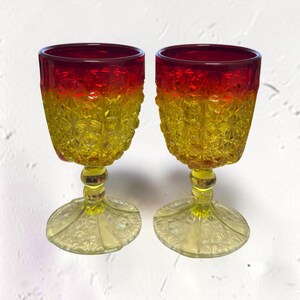 Puede incluir: Dos copas de cristal con un vibrante efecto degradado que transita desde un borde rojo intenso hasta una base amarilla brillante. Las copas y las bases circulares presentan un patrón geométrico de estrellas en relieve sobre un tallo amarillo.