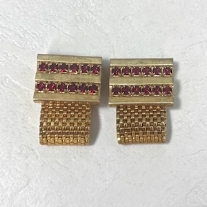 May include: A pair of gold-toned cufflinks with a rectangular top adorned with two rows of small, red gemstones. The lower portion features a woven gold mesh design, creating a classic and elegant accessory.