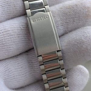 May include: A silver-toned Seiko watch band with a brushed metal finish. The band is composed of rectangular links and features the Seiko logo on the clasp. The watch band is shown against a white background.