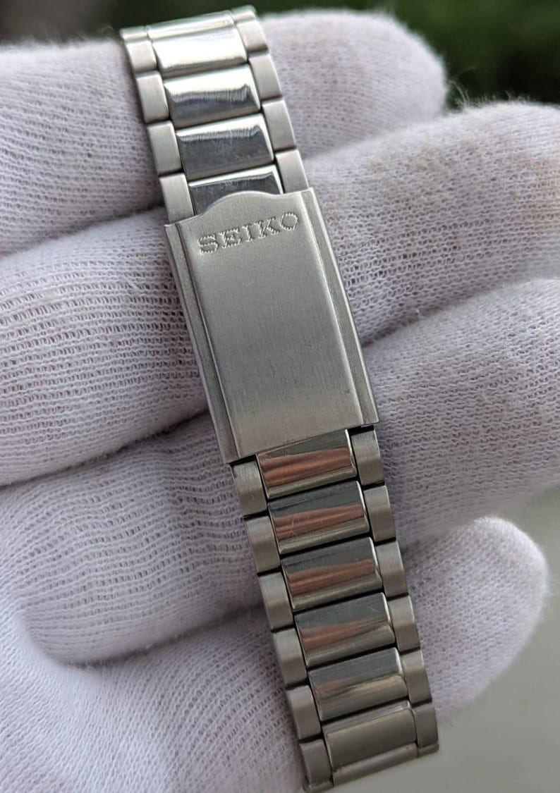 May include: A silver-toned Seiko watch band with a brushed metal finish. The band is composed of rectangular links and features the Seiko logo on the clasp. The watch band is shown against a white background.