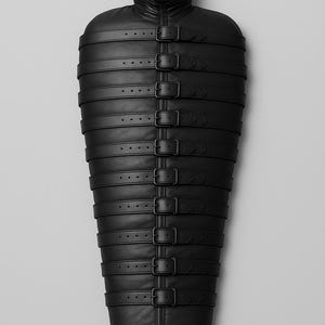 Könnte beinhalten: Ein schwarzes Lederkleidungsstück mit Kapuze und maskenartiger Gesichtsbedeckung. Der Körper ist umschlossen und durch mehrere horizontale Riemen mit Schnallen gesichert. Das Design ist symmetrisch und die Gesamtästhetik ist dunkel und minimalistisch.