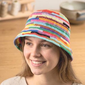 May include: A crochet bucket hat featuring a vibrant, multi-colored horizontal striped pattern. The hat is constructed with a dense, textured stitch and includes a wide, downward-sloping brim that encircles the head, showcasing a spectrum of colors.