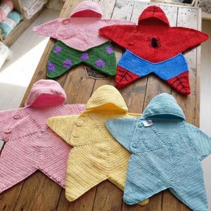 May include: Five star-shaped crochet baby blankets with hoods. One is pink with green polka-dot legs, one is red and blue with a spider emblem, and three are solid colors: light pink, yellow, and light blue. Each features two buttons on the front.