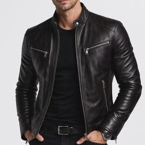 Op de afbeelding: Zwarte leren jas met een opstaande kraag en meerdere zakken met ritssluiting. De jas heeft een getailleerde pasvorm en een zilveren ritssluiting. Het model draagt een zwart T-shirt en een horloge.