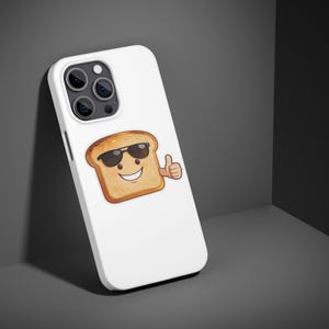 May include: White phone case featuring a cartoon image of a slice of toast wearing sunglasses and giving a thumbs-up. The toast has a smiling face and a golden-brown color. The phone case has a camera module with three lenses.