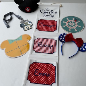 May include: A selection of Disney-themed items. Features a black Mickey Mouse ear hat, a lanyard with a Mickey Mouse character, a yellow and orange Mickey Mouse head cutout, a family organiser with names, and a headband with Mickey Mouse ears.