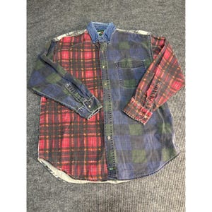 May include: A long-sleeved button-down shirt with a denim collar and a unique split design. One side features a red and black plaid pattern, while the other side has a blue, green, and black plaid. The shirt has a chest pocket.