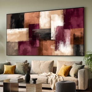 May include: Abstract rectangular wall art with a black frame. The artwork features a collage of rectangular shapes in shades of black, brown, white, and burgundy. The painting is displayed above a beige sofa with decorative pillows.