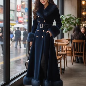 May include: A long, navy blue coat with a fur collar and cuffs. The coat features a double-breasted design with gold buttons and a matching belt. The coat is worn by a person standing near a window, with a blurred street scene visible outside.