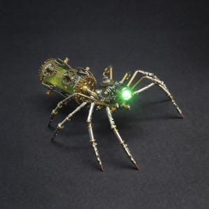 Puede incluir: Una escultura de araña de estilo steampunk con intrincados detalles de engranajes y metal. La araña tiene múltiples patas, un ojo verde brillante y un compartimento teñido de verde. La escultura está sobre un fondo oscuro.