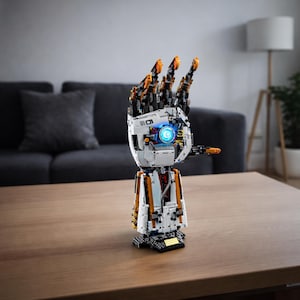 Op de afbeelding: Een gedetailleerd robotisch handmodel in wit, oranje en zwart, met beweeglijke vingers. Het model heeft een blauw oplichtend centrum en is gemaakt van in elkaar grijpende blokken, wat een mechanisch en technologisch ontwerp laat zien.