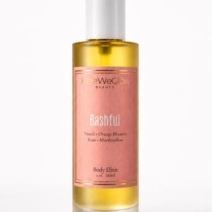 Bashful luxury body oil bottle with soft pink label and golden body elixir, designer inspired perfume oil aesthetic, moisturizing glow oil for women with feminine floral sweet scent profile.