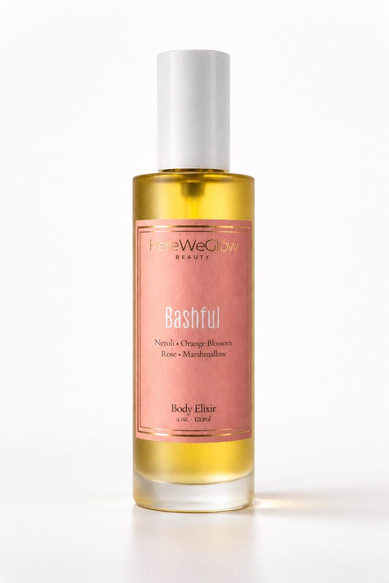 Bashful luxury body oil bottle with soft pink label and golden body elixir, designer inspired perfume oil aesthetic, moisturizing glow oil for women with feminine floral sweet scent profile.
