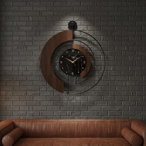 May include: A modern wall clock with a black marble face, gold hands, and a dark wood and metal spiral design. The clock is mounted on a dark gray brick wall above a brown leather sofa. A small light is above the clock.