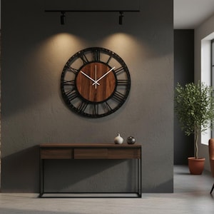 May include: A large, round wall clock with a black metal frame and Roman numerals. The clock face is made of wood. Below the clock is a dark wood console table with a black metal frame. The room has a modern, minimalist design.