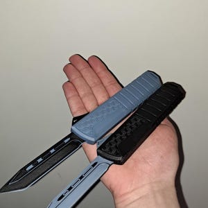 Könnte beinhalten: Zwei taktische Messer, eines hellblau und eines schwarz, werden gezeigt. Die Messer haben ein schlankes Design mit strukturierten Griffen und scharfen Klingen. Die Klingen haben ein einzigartiges Design. Die Messer werden in einer Hand gehalten.