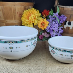 May include: Two white ceramic bowls with a turquoise and southwestern design. The bowls have a wide rim and a decorative band with geometric patterns and arrows. The bowls are of different sizes and are placed on a burlap surface.