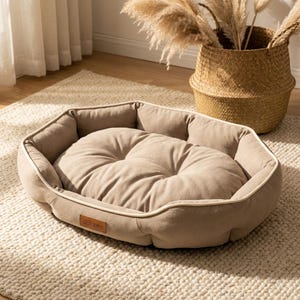 May include: A beige pet bed with a plush, button-tufted center cushion and a raised, padded rim. The bed has a light-colored trim and a small, rectangular label on the front. The bed is on a cream-colored rug.