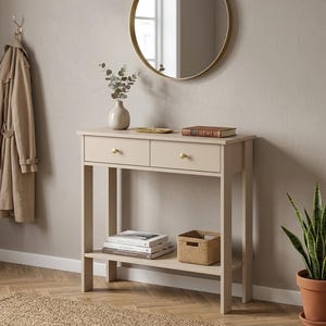 May include: A beige console table with two drawers featuring round gold knobs. The table has a lower shelf holding a stack of books and a woven basket. On the tabletop sits a ceramic vase with eucalyptus stems, a small gold tray, and a book.