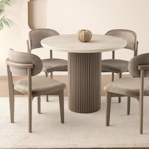 May include: A modern dining set featuring a round table with a textured top and a ribbed base. Four upholstered chairs surround the table, and a decorative vase sits on top. The set is placed on a light-colored rug.