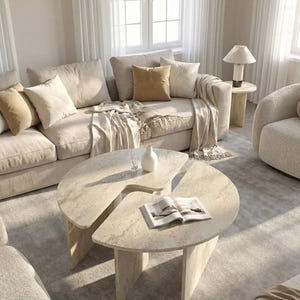 May include: A two-piece coffee table set featuring a light beige stone-like finish with a textured surface. The tables are semi-circular in shape, each supported by vertical panel legs, and are arranged to overlap slightly in a living room setting.