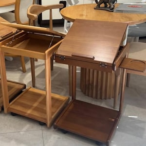 Puede incluir: Dos mesas auxiliares de madera con tapas con bisagras y estantes inferiores. Una mesa es de color marrón claro, la otra es de color marrón oscuro. Ambas tienen un pequeño estante lateral y ruedas. Otros muebles de madera en la habitación.
