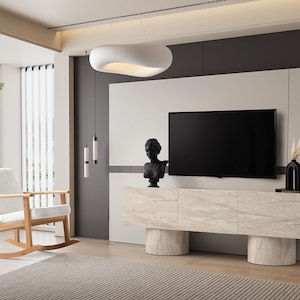 May include: A modern living room with a light-colored wooden rocking chair, a large flat-screen TV, and a marble-look cabinet. The room features a neutral color palette with a white ceiling light and decorative accents.