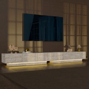 Puede incluir: Un mueble de televisión largo y de perfil bajo hecho de piedra travertino beige con una textura natural porosa. La unidad cuenta con seis puertas de armario, un diseño de base flotante con iluminación LED cálida integrada y una superficie plana.