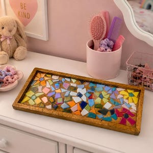 May include: A rectangular wooden tray featuring a colorful mosaic inlay made of various geometric glass pieces in shades of blue, yellow, orange, pink, and green. The tray has a natural wood frame and is positioned on a white surface.