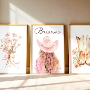 Op de afbeelding: Drie ingelijste wandposters. De linker poster toont een boeket roze bloemen vastgebonden met een lint. De middelste poster toont een persoon met lang haar en een roze cowboyhoed, met de naam Breanna erboven. De rechter poster toont twee lichtbruine cowboylaarzen omringd door kleine bloemen.